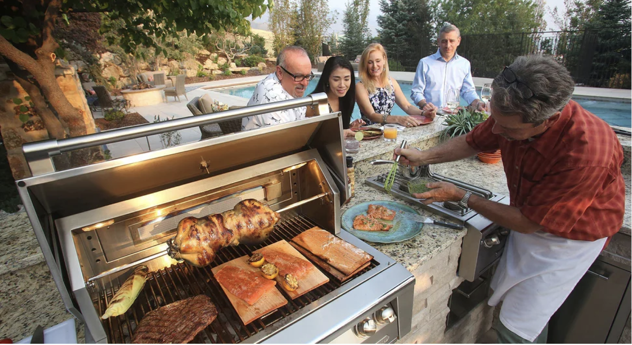 a grill being used on an outdoor patio by a pool with a man serving his friends salmon